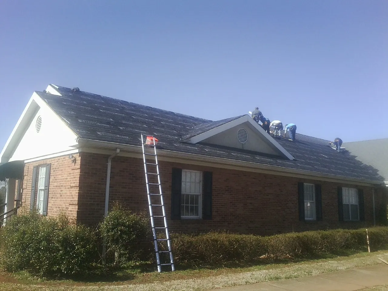 Crew tearing shingles off a brick ranch roof with a ladder set — Emergency Roof Repair work by our crew in Cades