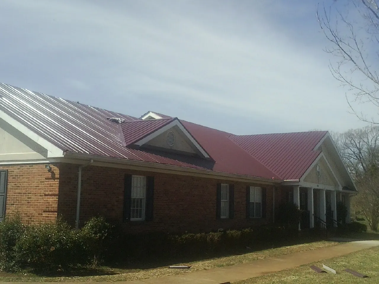 Red metal roof with gabled entries on a long brick building, from a Hail Damage Roof Repair job in Cades