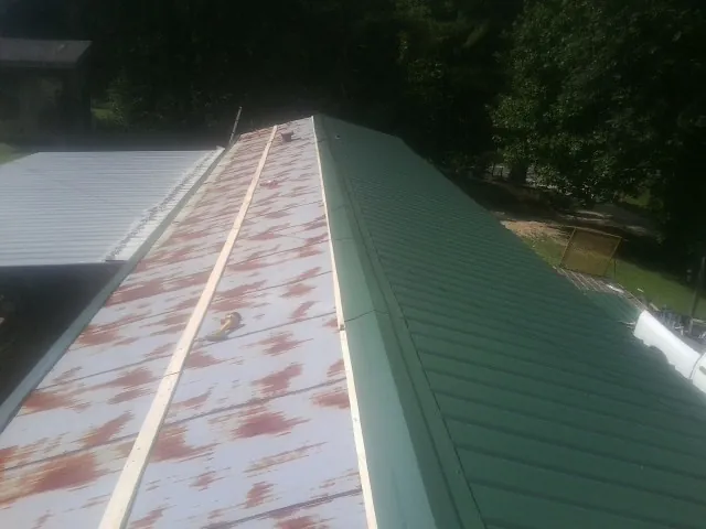Old rusted panels beside newly installed green metal roofing — Wind Damage Roof Repair by Roofing Brothers in Cades
