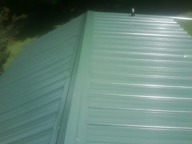 New green metal panels meeting at the ridge of a roof — Flat Roof Repair work by our crew in Cades