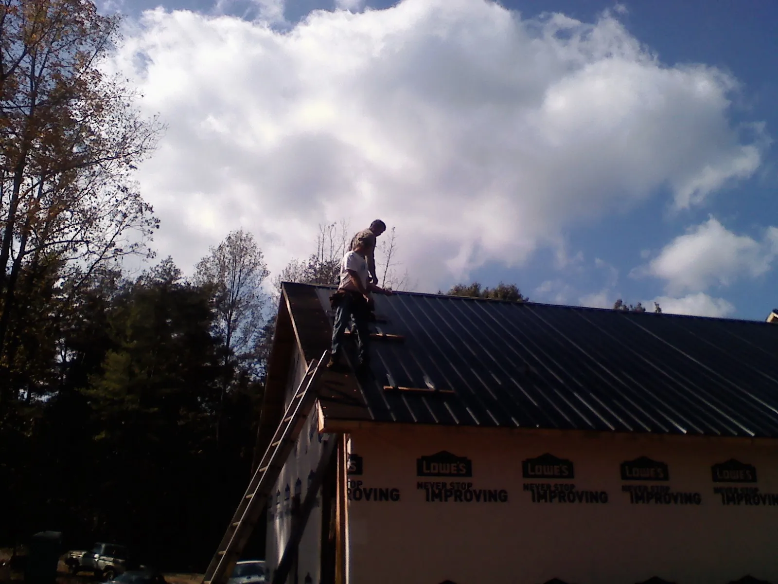 Roofer fastening dark metal panels high against a cloudy sky, from a Roof Inspection job in Cades