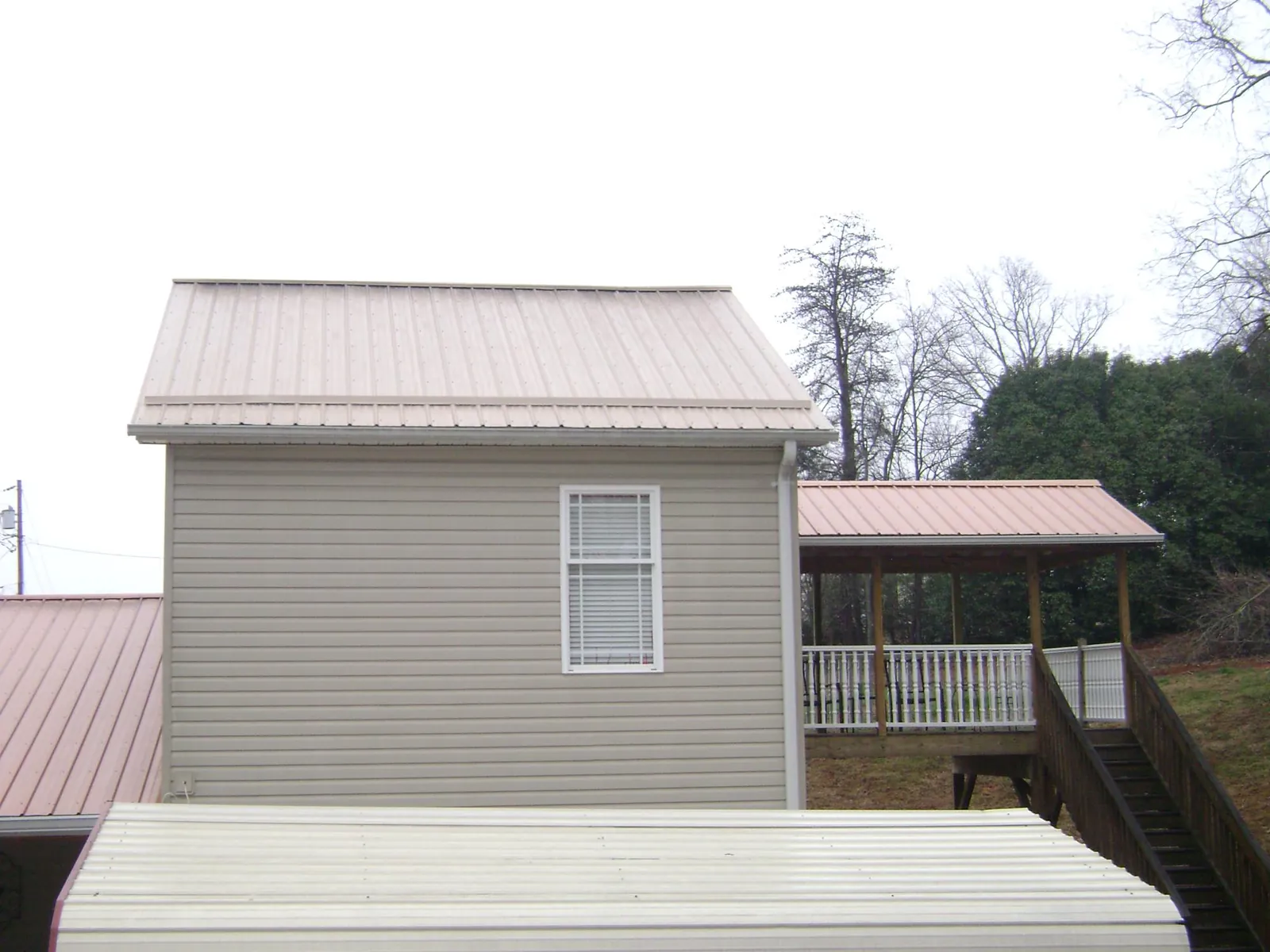 Tan metal roofs on a two story addition and attached porch, from a Roof Replacement job in Cades