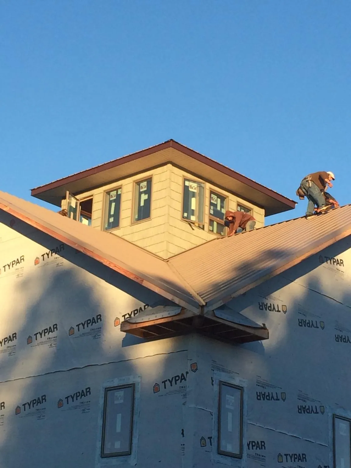 Roofers working around a rooftop cupola on a new metal roof at sunset — Roof Waterproofing in Cades by Roofing Brothers